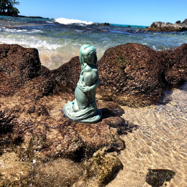 Mermaid dildo in front of lava rocks with blue crashing waves in background