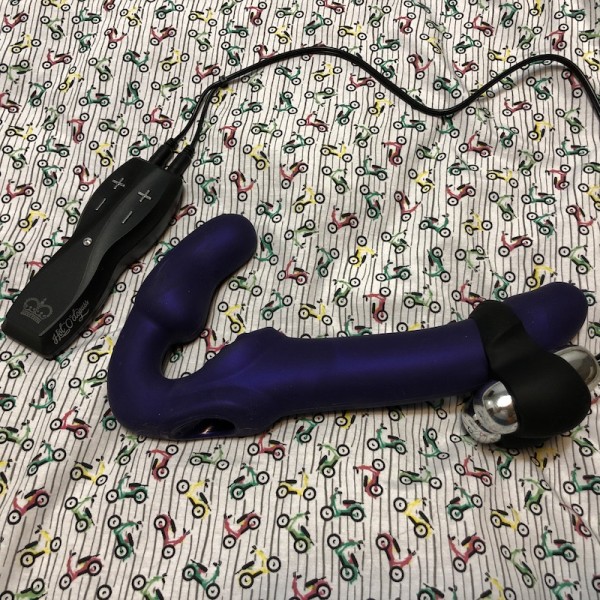 Jett penis vibrator attached to purple dildo on background of colourful scooter fabric