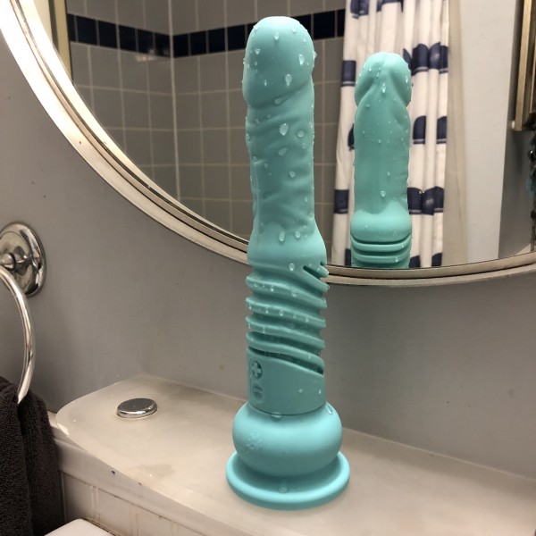Teddy dildo is on shelf in front of mirror. It is dripping wet with water.